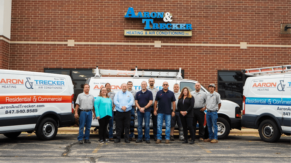 Ten people stand in front of Aaron & Trecker Heating & Air Conditioning, with two branded vans parked behind them outside a brick building.