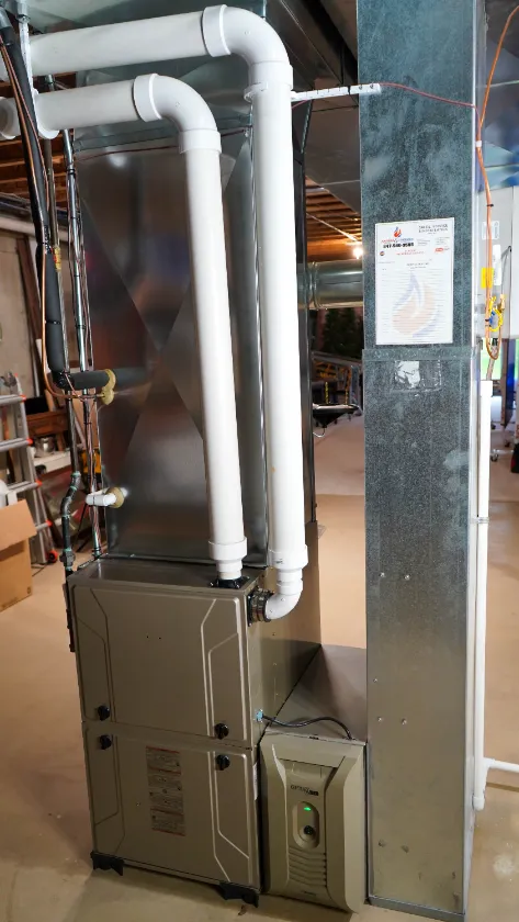 A modern HVAC furnace system with white PVC pipes installed in a basement, surrounded by unfinished walls and a concrete floor.